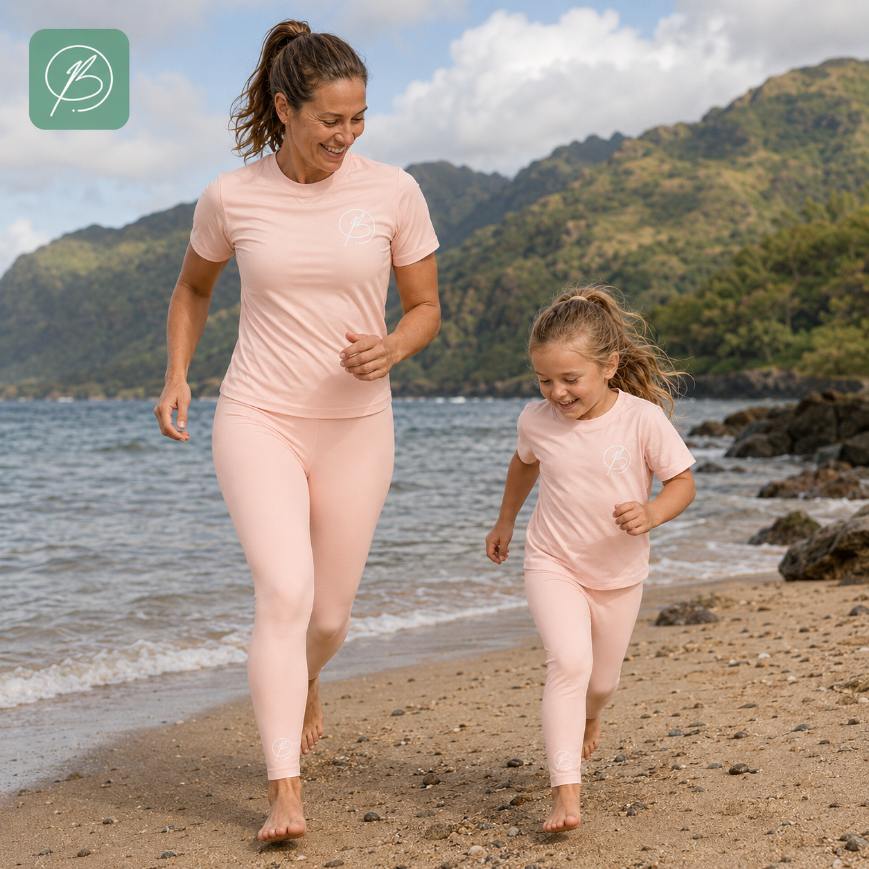 A woman and a child jogging on a sandy beach wearing matching light pink athletic sets, with ocean water and green mountains in the background. A small white logo is visible on the chest of both outfits, and a green square brand mark appears in the top-left corner.