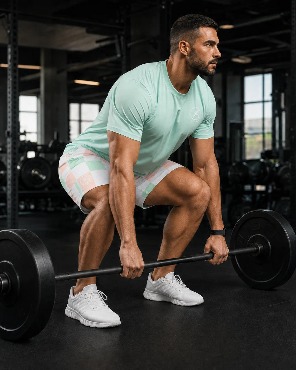 A man in a mint green t-shirt and patterned shorts lifts a barbell in a gym setting.