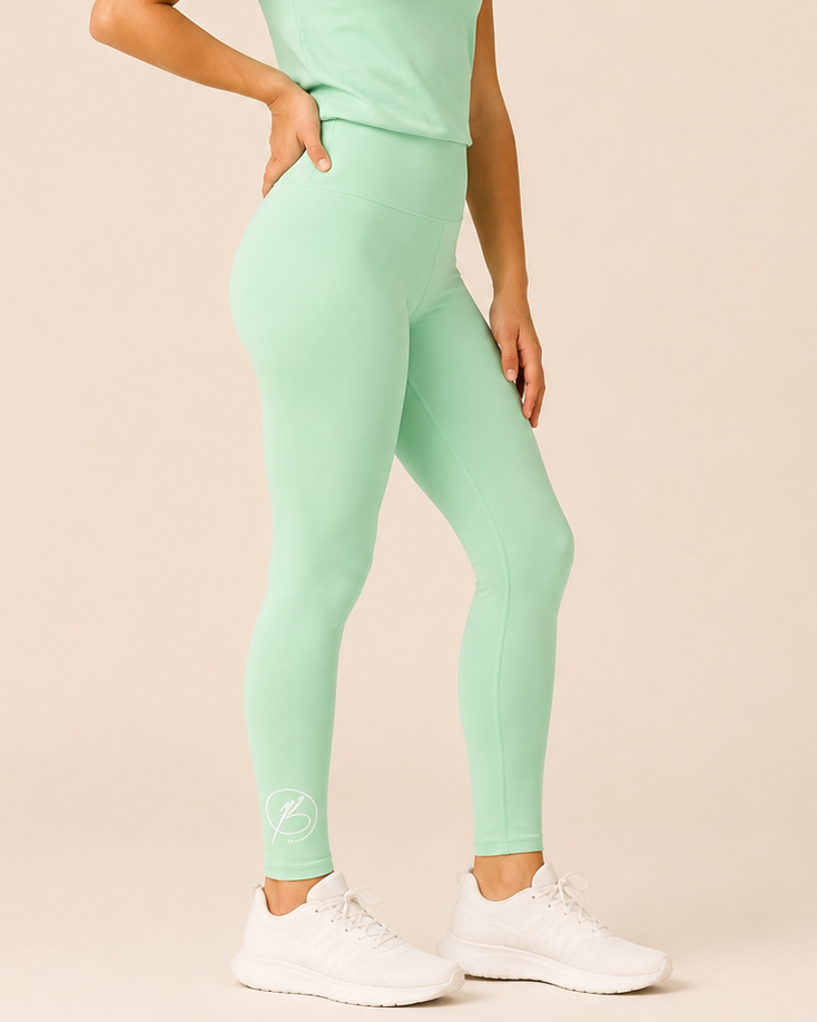 A woman modeling a mint green athletic set consisting of a short-sleeve t-shirt and high-waisted leggings, paired with white sneakers, against a solid beige studio background.
