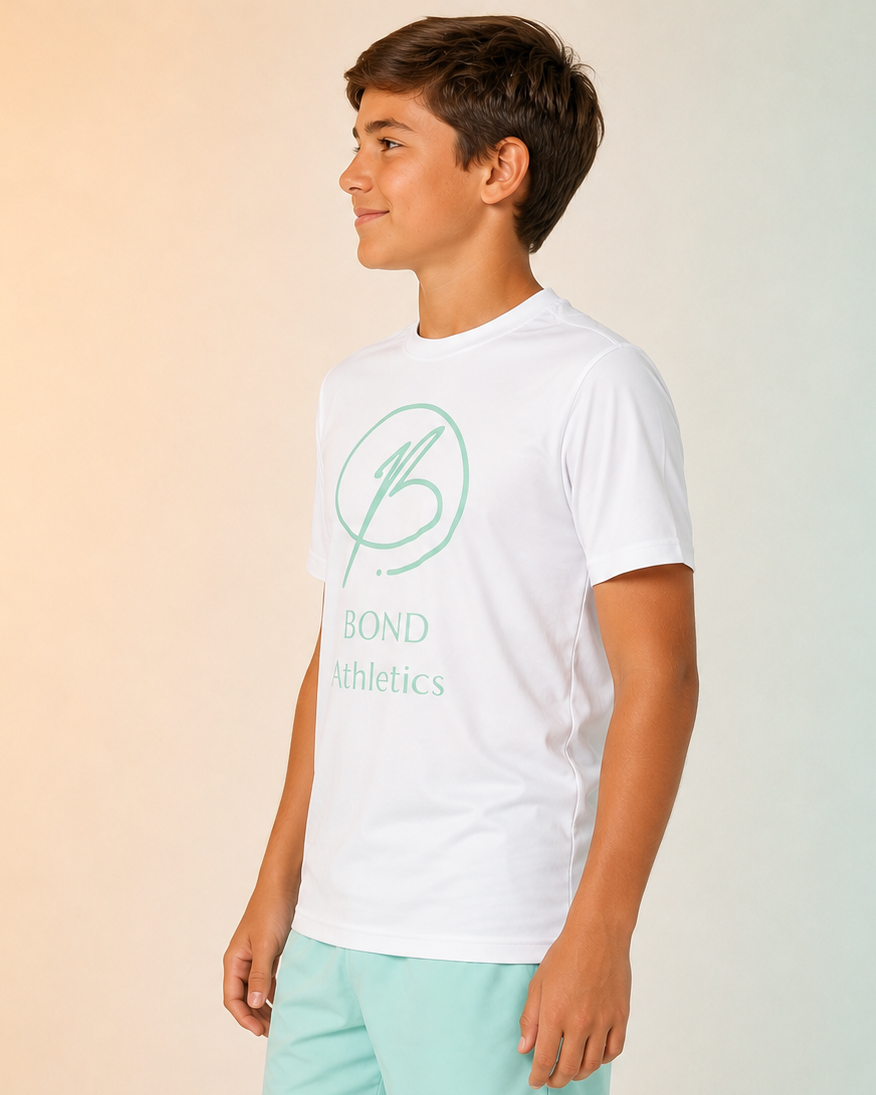 A boy modeling a white short-sleeve t-shirt with a mint green 'Bond Athletics' logo and matching mint green athletic shorts, set against a soft gradient background.
