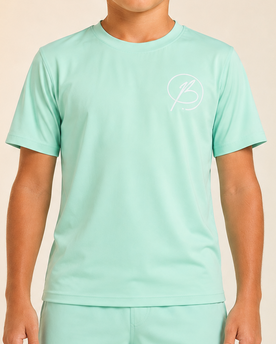 A child wearing a mint green athletic t-shirt and matching shorts with a small white circular logo on the chest and left leg, set against a soft beige studio background.