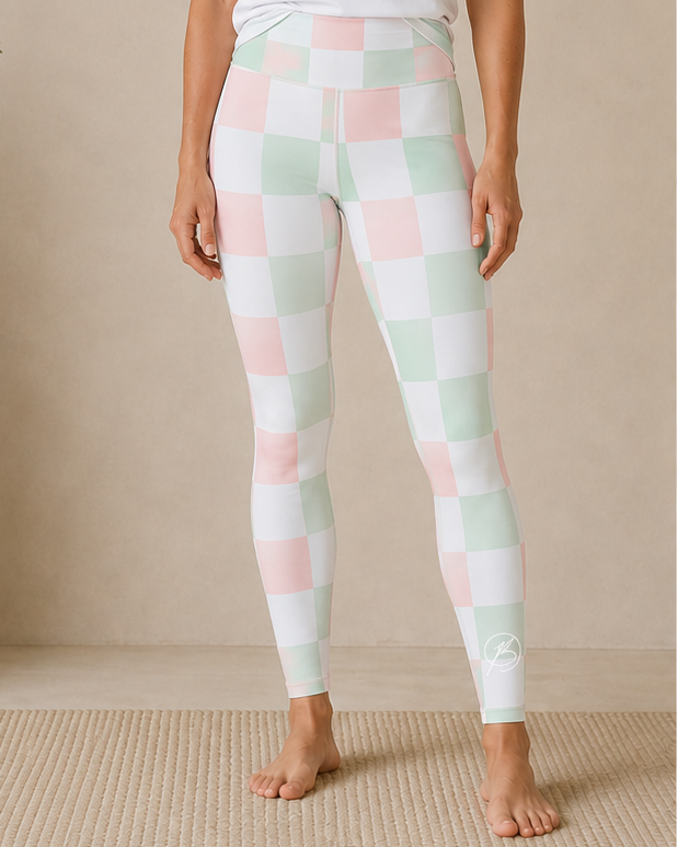 A woman stands barefoot indoors wearing a white short-sleeve athletic T-shirt with a mint green 'BOND Athletics' logo and pastel checkered leggings in white, pale pink, and mint green.