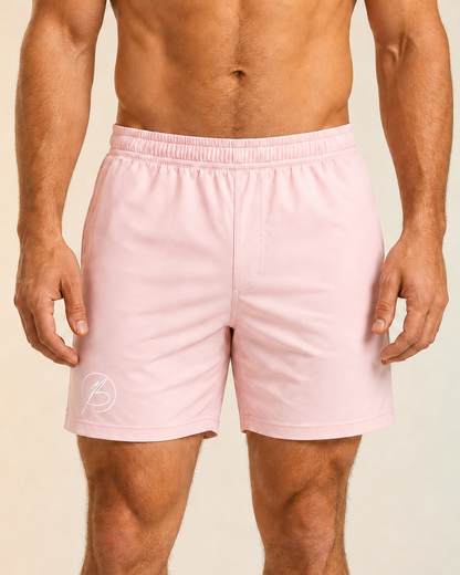 A man wearing light pink athletic shorts with an elastic waistband and a small white circular logo on the lower left leg, shown from the waist down against a soft beige studio background.